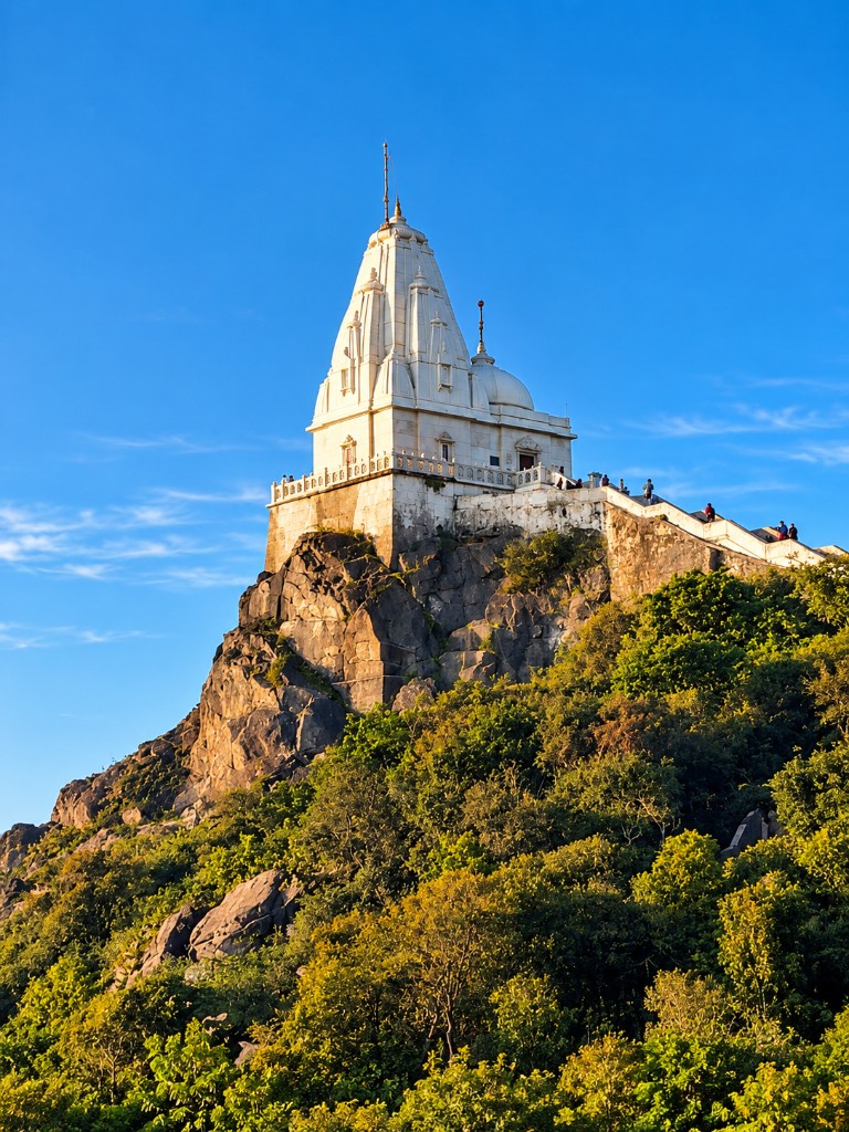White Shikharji Jain temple on the rocky peak of Parasnath Hill against a clear blue sky